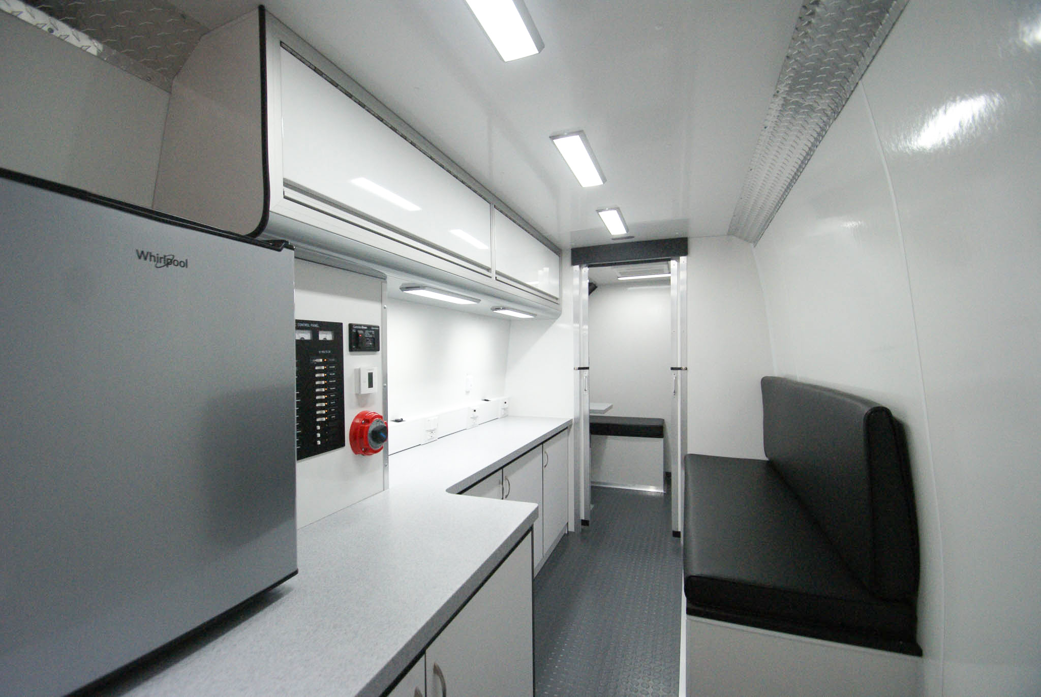 An angled view of the Mobile Outreach sprinter van's back room that also features the refrigerator, electric control panel, and overhead cabinets. Through the open doors, you can see the waiting area.