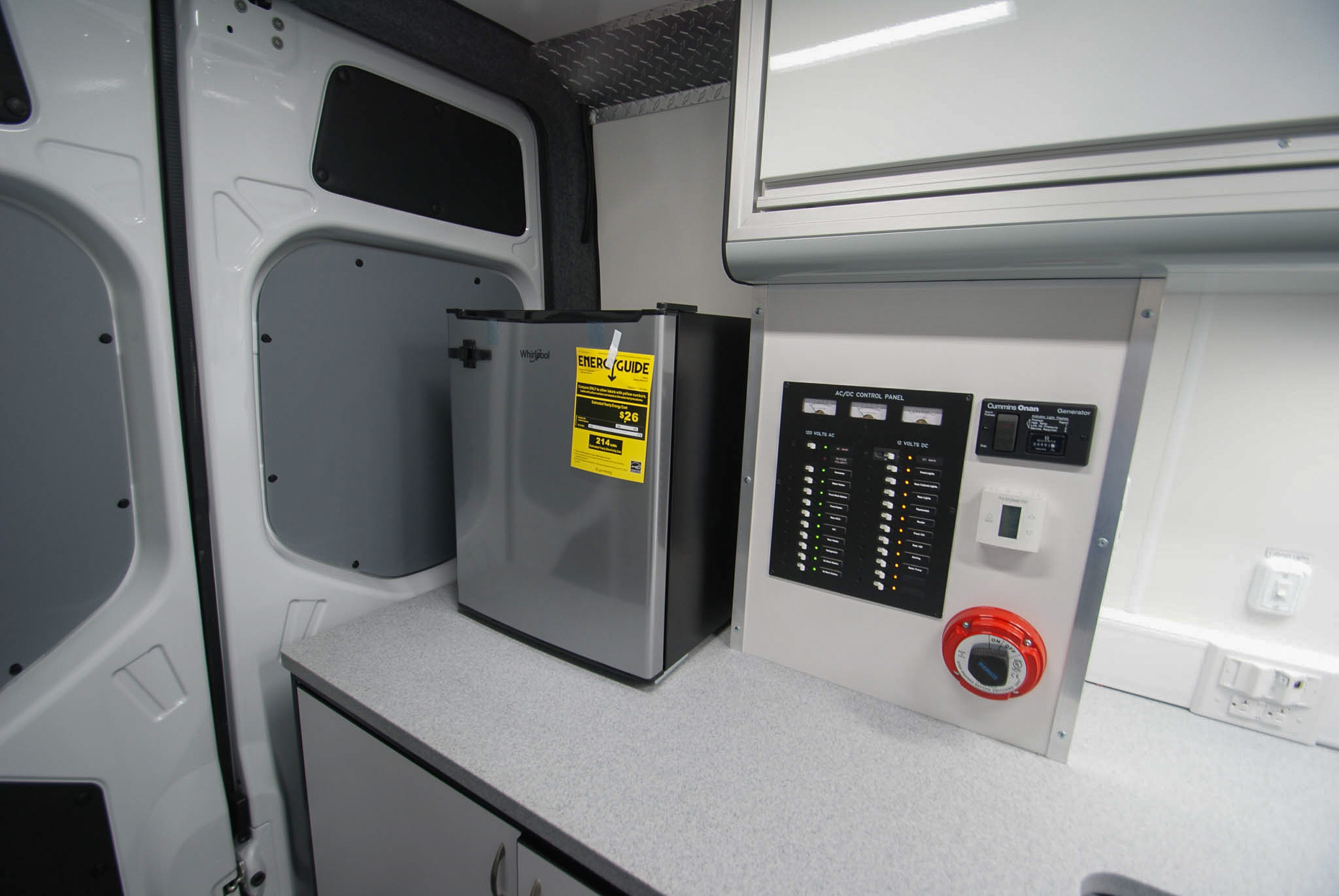 An up close view of the refrigerator and electric control panel in the Mobile Medical Exam sprinter's back room.