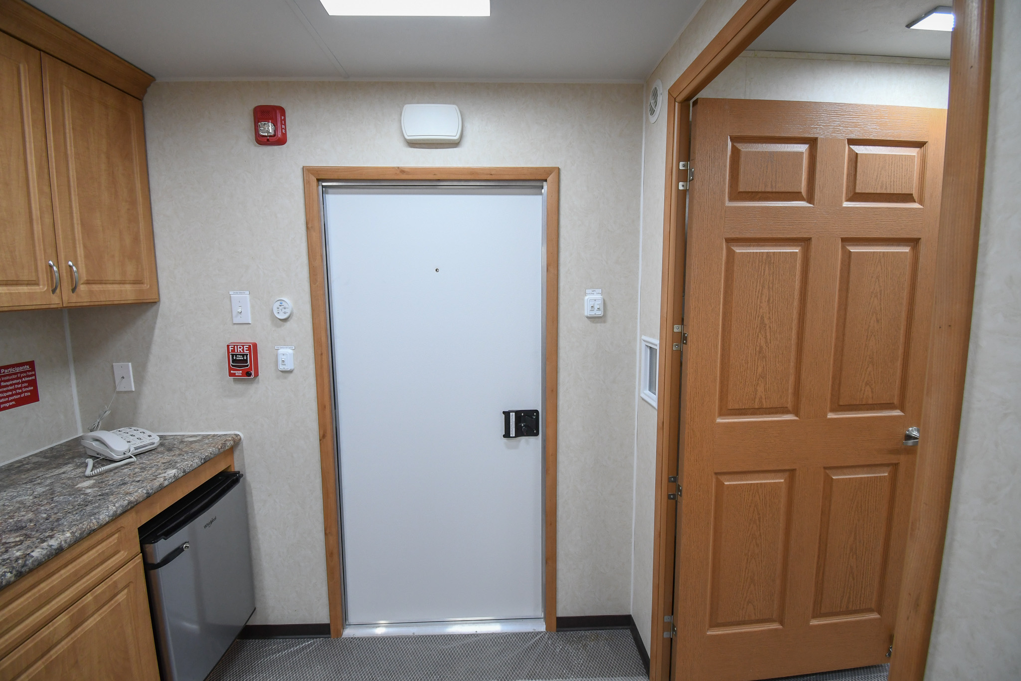 A view of the refrigerator, exit, phone, and pull station inside the units for Sandy, UT.