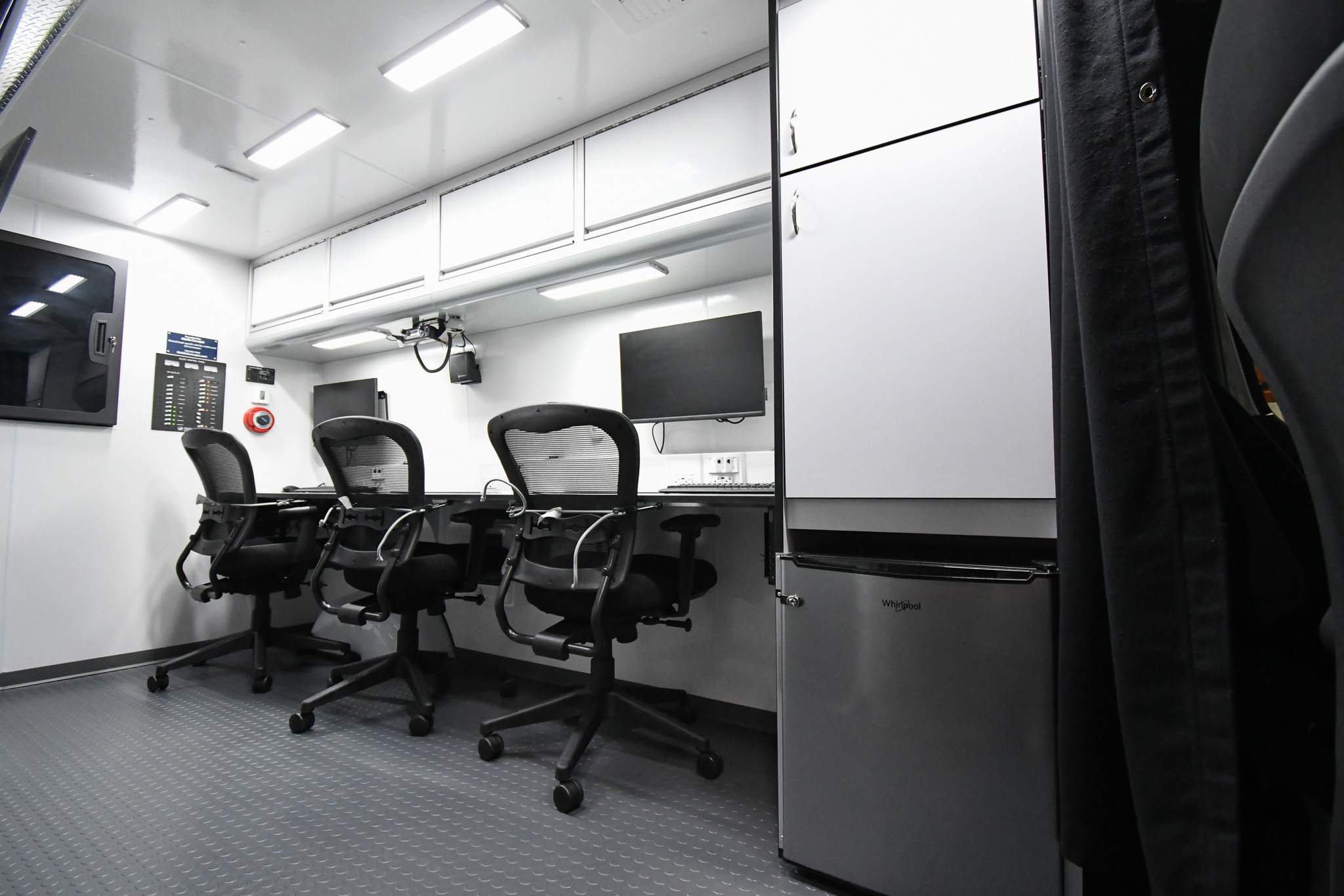An interior view of the 3 workstations, refrigerator, cabinets, and wall-mounted electronics rack cabinet inside the unit made for the San Joaquin County Sheriff's Office.