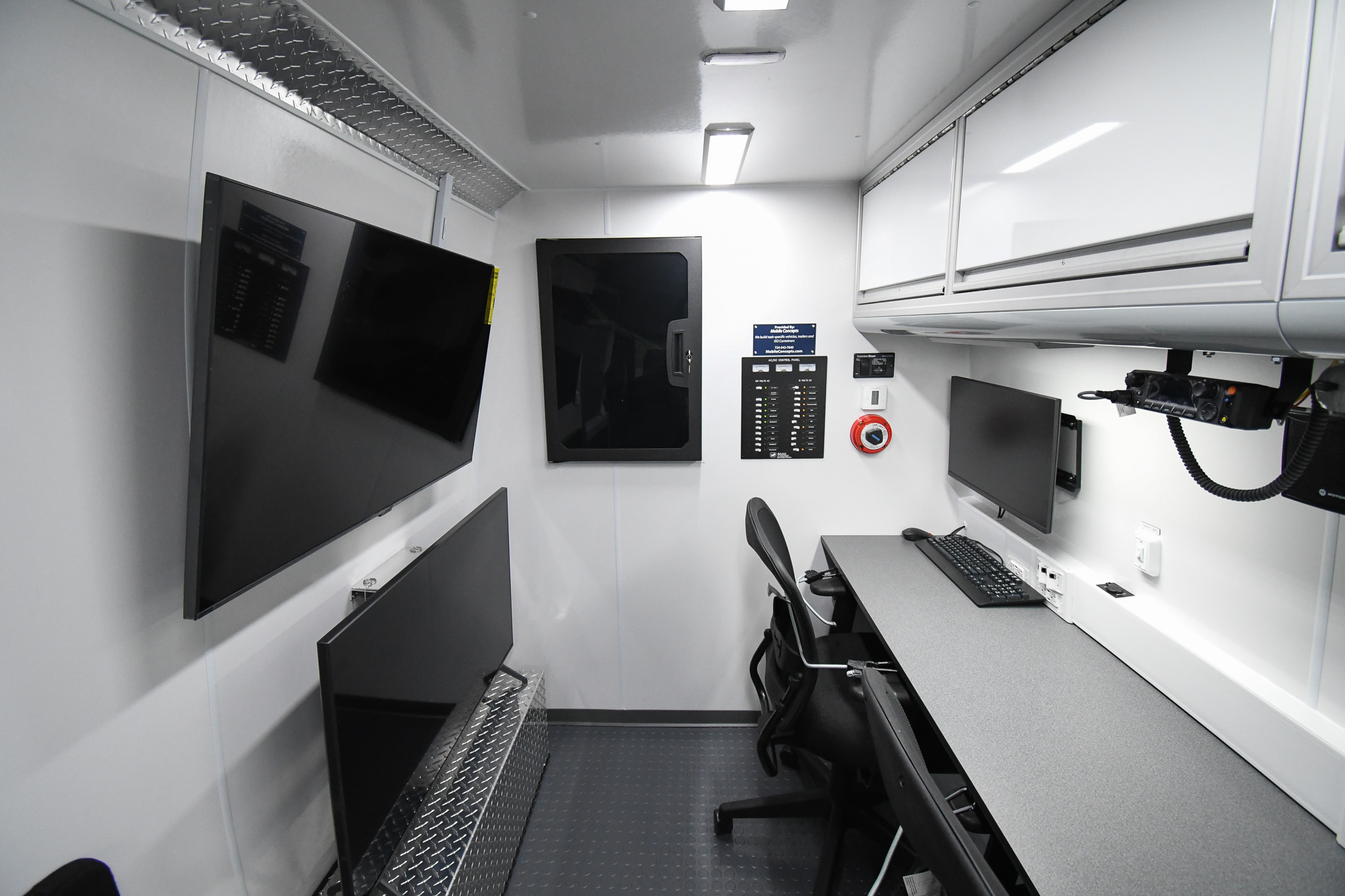 An interior view of 2 workstations, 2 TVs, and the wall-mounted electronics cabinet inside the unit made for the San Joaquin County Sheriff's Office.