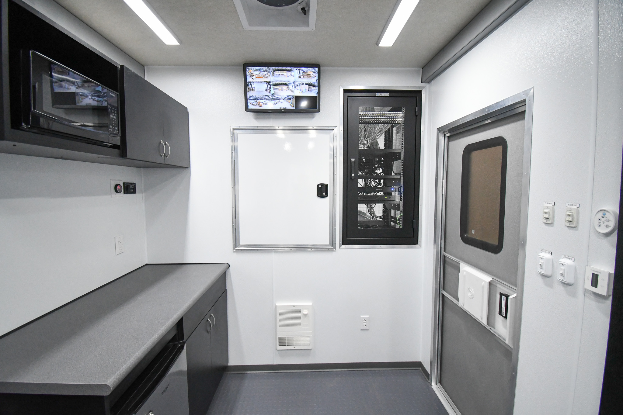 A view showing an exit, galley, electronics rack, overhead monitor, and doorway to the 5th wheel storage inside the unit for Hillsborough, NC.
