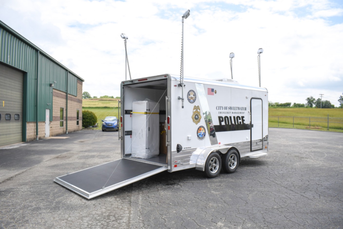 An exterior view of the Command 20 Cargo Supply trailer made for Sweetwater, FL. The push-up pole lights are up, and the rear ramp door is down.